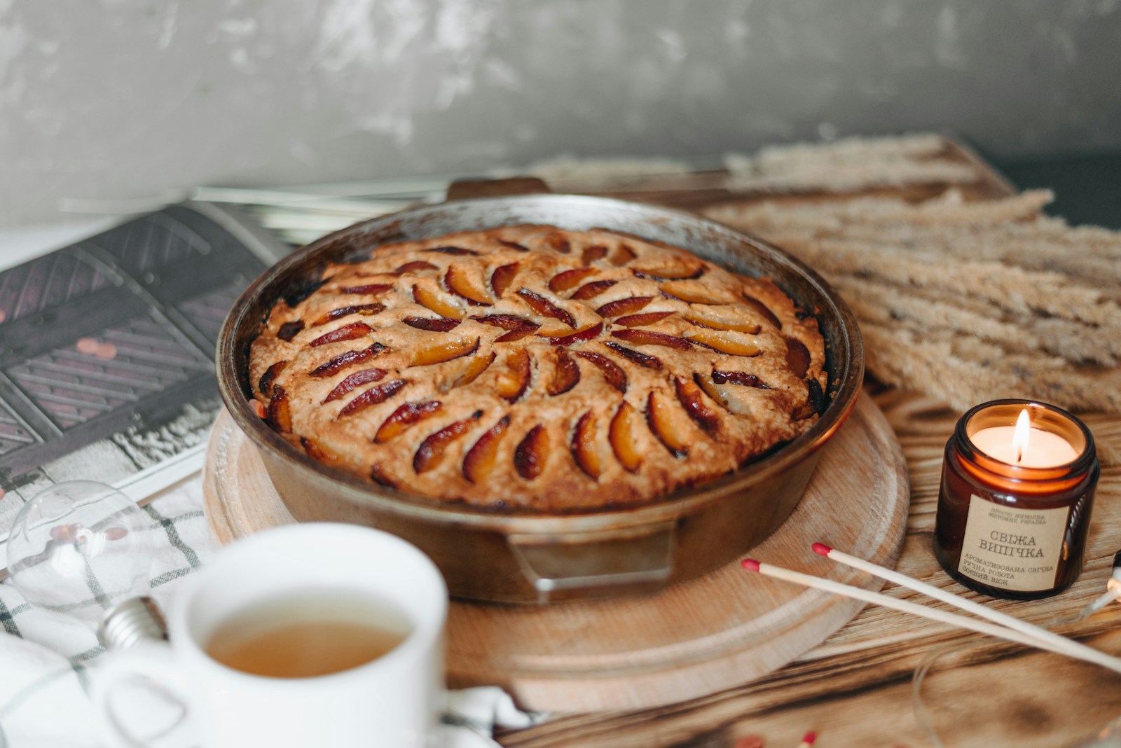 baked pie in round tray near lighted scented candle, light bulb, and white ceramic teacup